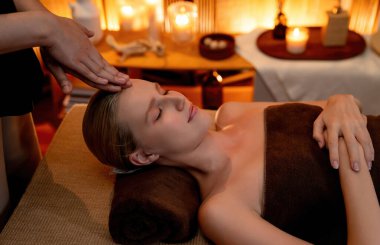 Beyaz kadın stres önleyici kafa masajı yapmaktan ve lüks otel veya otelde sıcak mum ışığında yüz güzelliği eğlencesi yapmaktan zevk alıyor. Sessiz.