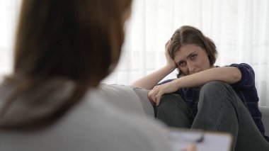 Psikologla ruh sağlığı terapisi gören üzgün travma sonrası stres bozukluğu olan bir kadın. Yaşam sonrası depresyon veya keder. Hayal kırıklığına uğramış genç bir kadın klinikteki duygular hakkında prim psikoloğuyla konuşuyor.