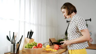 Enerjik anne, mutfak malzemeleri ile çevrili sebzeleri doğrarken modern mutfakta kahvaltı için salata yapıyor. Akıllı kadın temizlikçi yemek pişirir ve yemek hazırlar. Sağlıklı bir yaşam tarzı. Pedagoji.