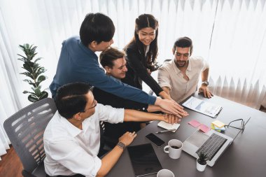 Çeşitli ofis çalışanlarından oluşan bir grup, ofis odasında el ele vererek iş sinerjisini ve iş yerindeki güçlü verimli takım çalışmasını sembolize ediyor. İş çalışanları arasındaki işbirliği ve birlik. Tedbirli