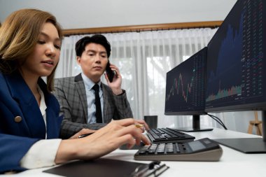 Gülümseyen Asyalı işadamı komisyoncu dinamik borsa veritabanını arıyor. Kadın iş ortağı, iç işyerindeki kar eden uygulama programını karşılaştıran ekranlara işaret ediyor. İnfobahn.