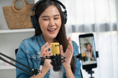 Asyalı sunucu canlı yayında canlı yayında canlı yayında sosyal medyada kulaklık takarak konuşuyor. Dinleyicileri modern stüdyoda koçluk yaparak selamlıyor. Taktik.