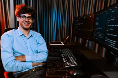 Ekranda yazılım geliştirme bilgisine karşı oturan gülümseyen bilişim geliştiricisinin profili, web sitesindeki son sürüm uygulaması için program kodlaması oluşturarak çevrili kameraya bakıyor. Toplayıcı.