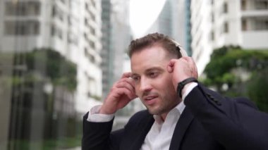 Kafkasyalı iş adamı cep telefonunu tutarken rahatlatıcı müzik dinliyor. Yetenekli mutlu yönetici müzik açar ve yeşil şehir veya parkta otururken neşeli bir şekilde şarkıya geçer. Urbane.
