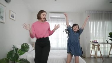 Yatak odasında Asyalı kızıyla müzik eşliğinde dans eden mutlu çekici anne. Beyaz anne dans eder ya da egzersiz yapar. Bu arada tatlı çocuk da müzik eşliğinde yatağa atlar. Aile eğlence konsepti. Pedagoji.