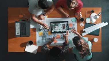 İnşaat mühendislerinin masa başında proje planıyla otururken tablet kullanarak ev yapısını dizayn etmelerine tepeden aşağı bir bakış açısı. Ekip planlama ve inşaat hakkındaki fikirlerin havadan görüşü. Sempozyum.