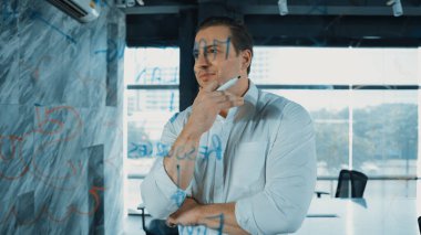 Akıllı iş adamı cam tahtanın önünde bir proje başlatmayı düşünüyor. Gülümseyen erkek proje yöneticisi yaratıcılık pazarlama stratejisini gösteren renkli yapışkan notlara bakıyor. Yönlendirici.