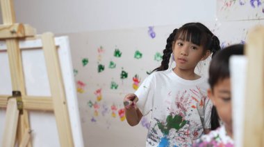 Oyuncu öğrenci resim dersinde ya tuvali boyadı ya da boyadı. Lekeli duvarda el iziyle dururken beyaz gömlek giyen Asyalı bir kız. Yaratıcı aktivite. Etkinlik.