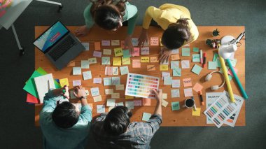 Gündelik kıyafet giyen, dizüstü bilgisayara bakan ve fikir paylaşan iş ekibinin zaman atlaması. Yapışkan notlar ve kulaklıkla masada çalışan ve renk paletini kontrol eden yöneticinin hava görüntüsü. Sempozyum.