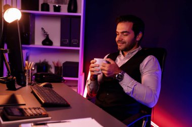 Gülümseyen zeki işadamı, elinde kahve fincanı olan satış ekibiyle buluşuyor ve geceleri Mor Neon Light Home Office 'deki bilgisayar ekranında ürün hedef pazarını araştırıyor. Tahmin et..