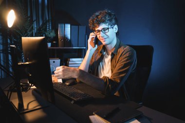 Genç iş adamı akıllı telefondan müşteriyi ya da iş arkadaşını arıyor, neon modern ofisteki yaratıcı sunum surround çalışma masasının bilgisayar ekranına bakıyor. Yeni proje kavramı. Toplayıcı.