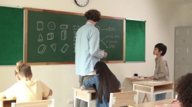 Asyalı çocuk cevap yazmayı bitirirken öğretmen de çocuğu teşvik etmek için el çırpıyor. Öğretmen matematik dersinde öğrenciyi alkışlarken ve el çırparken çekici öğrenci koltuğuna geri dönüyor. Pedagoji.