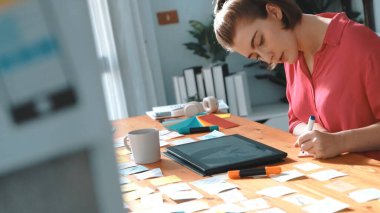 Tablet ekran logosu tasarımı ile toplantı masasında otururken renkli yapışkan notlar üzerine tasarımcı yazma fikrinin üst görünümü. Tasarım yapan ve karar veren profesyonel bir iş kadını. Sempozyum.