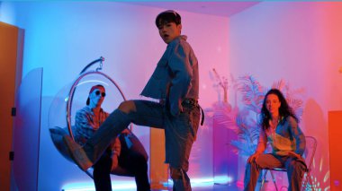 Çok kültürlü bir arkadaş kürsüde otururken Asyalı yetenekli bir dansçı modern müziğe geçiyor. Profesyonel dansçı, hipster takımı tezahürat yaparken ve desteklerken enerjik adımlar atıyor. Mutluluk.