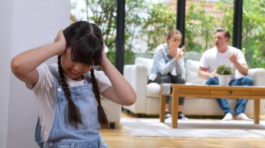 Stresli ve mutsuz genç kız köşeye kıvrılıp kulaklarını kapatarak arka planda ebeveyninin tartışmasını engelliyor. Evde aile içi şiddet ve travmatik çocukluk depresyona dönüşür. Eşzamanlama