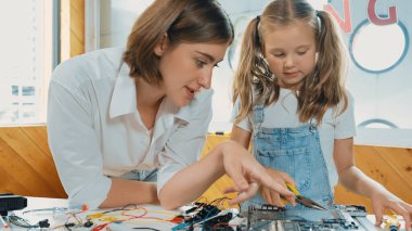 Genç, zeki, beyaz bir öğretmen öğrencilere elektronik kurulun bir parçasını öğretiyor. Uzman kız dijital elektrikli aletleri öğreniyor ve cips ve kablolarla ana kartı tamir ediyor. Etkinlik.