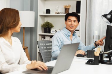 Gülümseyen Asyalı bir adam, yan görüntüdeki modern ofis çalışma masasında veri tabanını ararken günlük dizüstü bilgisayarla pazarlama raporu projesini planlarken kadın meslektaşıyla konuşuyor. İnfobahn.