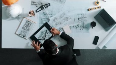 Akıllı mühendisin giysi giymesi ve inşaat malzemelerini kontrol ederken tablete bakması. Mimarların bina inşaatının yukarıdan aşağıya doğru görüntüsü planlara bakarken. Hizalama.