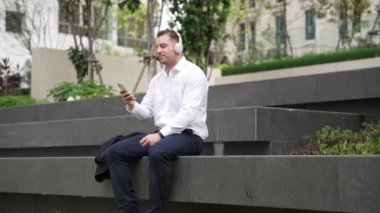 Zeki iş adamı, takım elbisesini çıkarırken rahat müzik dinlemek ve Green City 'de müzik dinlemek için kulaklık takar. Canlı şarkıyla kulaklık dansı yapan mutlu proje yöneticisinin yan görüntüsü. Urbane.