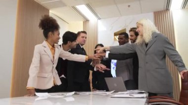 Çeşitli ofis çalışanları, işyerindeki iş sinerjisini ve üretken takım çalışmasını sembolize eden süslü ofis odasında el ele tutuşuyorlar. İş çalışanları arasındaki işbirliği ve birlik.