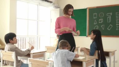Zeki Asyalı öğrenci, ilkokulda öğretmen yürürken ve ödevlerini kontrol ederken matematik sorusunu sorarak elini kaldırdı. Öğretmen not defterini alırken soruyu cevaplıyor. Pedagoji.