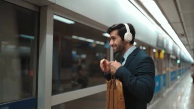 Tren platformda hareket ederken akıllı proje yöneticisi kulaklıktan müzik dinliyor. Kafkasyalı iş adamı kulaklık kullanıyor. Platformda beklerken rahat müzik dinliyor. Çalışma rutini. Sevinçli..