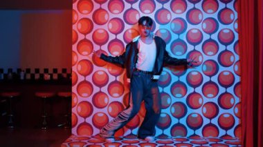 Asyalı break dansçı serbest stile geçiyor ve balon arka planlı kameraya bakıyor. Profesyonel hippi gündelik kıyafet giyer ve gözlük takar. Mutluluk.