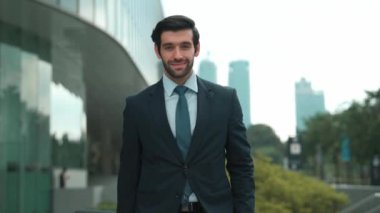 Profesyonel iş adamı hareket ediyor ve kameraya bakarken ayakta duruyor. Gülümseyen yönetici kameraya kendinden emin bir şekilde gülümsüyor. Mimari binada takım elbiseli yatırımcıların yakın çekimi. Sevinçli..