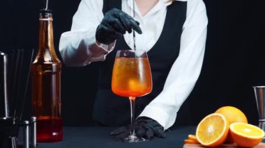 Makrografi, bir barmenin yetenekli ellerine tanık olun. Aperol Spritz kokteylinde dikkat çekici bir siyah arka plana karşı ustalıkla buz karıştırıyorlar. Her yakın plan el yapımı kokteyl. Geliştirilebilir.