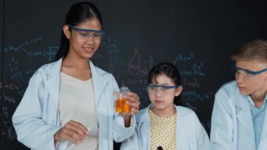 Değişik öğrenciler masada mikroskop ya da tüpü sıvıyla karıştırırken renkli solüsyonları karıştırıyorlar. Kimyasal teorisiyle karatahtanın önünde duran Asyalı kız deney tüpü tutuyor. Öğretim