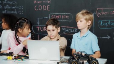 Çocuğun dizüstü bilgisayar mühendisliği kodunu ve yazım programını kullanırken bir grup zeki öğrencinin etrafı STEM teknoloji sınıfında arkadaşlarıyla çevriliyken karatahtaya oturması. Etkinlik.