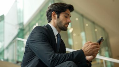 Akıllı proje yöneticisi merdivenlerde otururken cep telefonuna bakıyor. Çekici Kafkasyalı iş adamı telefon kullanarak çalışıyor. Profesyonel yatırımcı iş stratejisi planlamak için telefonu kullanıyor. Sevinçli..