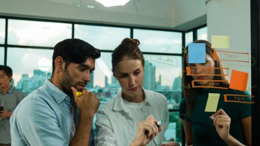 Profesyonel iş adamları beyin fırtınası yapıyor, fikir paylaşıyor, düşünüyor yetenekli erkek liderler cam duvarda yapışkan notlar yazarken. Yetenekli yönetici ofisteki cam duvara iş planı koymuş. İzleme