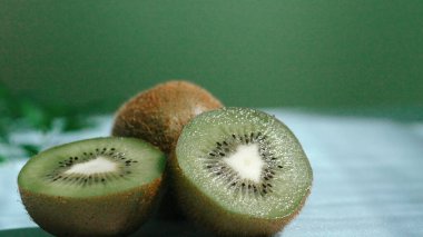 Islak zeminde dilimlenmiş kivi meyvesi ve yeşil arka planda yakın plan. Makro taze kivi ve su dalgalı dilimlenmiş kivi. Sağlıklı beslenme ve doğal gıda kavramı. Poster için tasarım, duvar kağıdı. Pabulum.