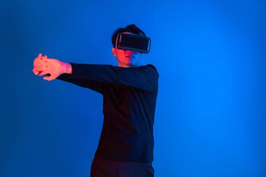 Zeki sporcu VR giyip tüm vücudunu mavi neon ışıklı arka plan üzerinde gererek dijital fütüristik teknoloji sanal gerçekliğini egzersiz konseptine bağlıyor. Entrika.