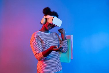 Canlı dijital fütüristik teknoloji meta metasında hologram uygulaması güzellik bezi ürünü üzerinde alışveriş poşeti tutarken İnternet üzerinden alışveriş yapan genç Afrikalıların keyfini çıkarın. Entrika.