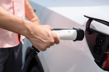 Dışarıdaki şarj istasyonundan EV şarj aletini şarj etmek için elektrikli araca elle tak. Alternatif temiz ve sürdürülebilir enerji kavramına sahip taze gün ışığı ortamı. Kalıcı