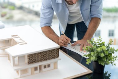 Modern ofisteki mimari aletleri kullanarak ev modelini ölçen profesyonel mühendisin portresini yakından çek. Ev inşaatı, bina planı. Üst Manzara. Eline odaklan. İzleme.