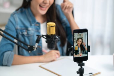 Asyalı sunucu canlı yayında canlı yayında canlı yayında sosyal medyada kulaklık takarak konuşuyor. Dinleyicileri modern stüdyoda koçluk yaparak selamlıyor. Taktik.