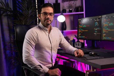 Bilgisayar ekranındaki yazılım geliştirme kodlamasına karşı poz vermek için akıllı bilişim geliştirici görünümlü kamera profilleri, neon ışıklı siber oda ofisinde program güncellemesi internet sitesi verileri sunuyor. Tahmin et..