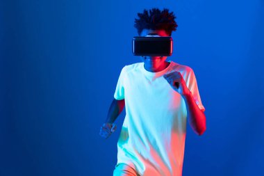 Genç Afrikalı Amerikalı spor koşucusu VR ile egzersiz koşusu koşusu yapıyor mavi neon duvarda yarış koşusu yapıyor metaevren dünyasındaki fütürist teknoloji sanal gerçekliğini birbirine bağlıyor. Entrika.