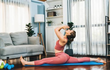 Spor kıyafetleri içinde esnek ve becerikli bir kadın evde egzersiz paspası üzerinde meditasyon pozisyonunda yoga yapıyor. Huzurlu ve huzurlu bir yoga yaşam tarzı..