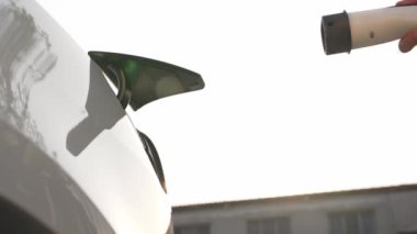 Ağır çekimde çalışan adam, alışveriş merkezinin otoparkındaki kamu EV şarj istasyonunda elektrik için akıllı telefon kullanıyor. EV aracıyla modern çevre ve sürdürülebilir kentsel yaşam tarzı