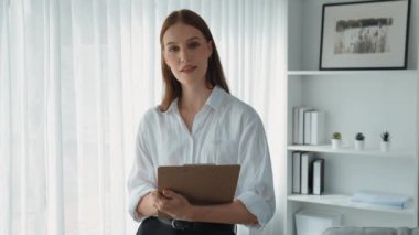 Klinikteki dost canlısı psikolog kadın. Profesyonel portresi. Kameraya bakıp psikolog muayenehanesine bakıyor. Tecrübeli ve kendinden emin psikolog.