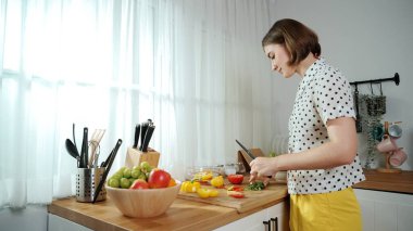 Enerjik anne, mutfak malzemeleri ile çevrili sebzeleri doğrarken modern mutfakta kahvaltı için salata yapıyor. Akıllı kadın temizlikçi yemek pişirir ve yemek hazırlar. Sağlıklı bir yaşam tarzı. Pedagoji.