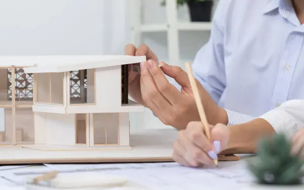 stock image Professional male engineer hand measure house model by using ruler while beautiful cooperative coworker working together by writing on blueprint. Creative design and teamwork. Closeup. Immaculate.