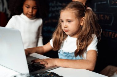 Beyaz önlüklü sarışın kız BTMM sınıfında kendine güvenen dizüstü bilgisayar kullanarak robot teknolojisini öğreniyor. Beyaz süveter giyen kız meraklı gözlerle kodlamasına bakıyor. Etkinlik.