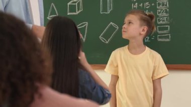 Profesyonel öğretmen konuşuyor ve sınıfta Asyalı çocuğa fikrini açıklıyor. Sınıfın önünde karatahta matematik dersiyle dikilmiş beyaz öğrenci dinleme eğitmeni. Pedagoji.