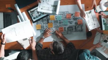 Planı elinde tutan inşaat mühendisi ekibinin en iyi görüntüsü ve dizüstü bilgisayar, proje planı ve planıyla masada duruyor. Yapışkan notları planlayan ve yazan yetenekli proje yöneticisinin havadan görünüşü. Sempozyum.