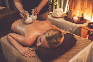 Sıcak bitkisel top spa masaj vücut tedavisi, masör kadın vücuduna nazikçe şifalı bitki torbası bastırıyor. Aromaterapi tesisinin sakinliği ve dinginliği kaplıca salonundaki mumların sıcacık ışığında. Sessiz.
